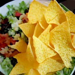 the taco salad is transferred to a plate and topped with cheddar cheese and tortilla chips.