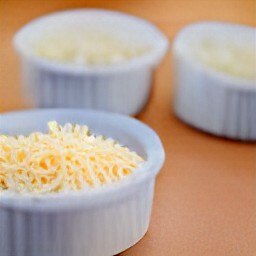 the egg mixture is transferred to the ramekins and topped with grated cheese. the ramekins are then placed on a baking sheet.