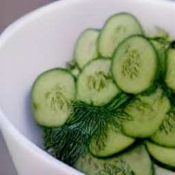 a bowl of drained cucumbers with chopped fresh dill sprinkled on top.