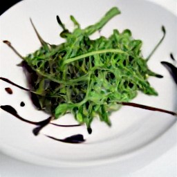 a plate of arugula and balsamic vinegar that has been combined with a fork.
