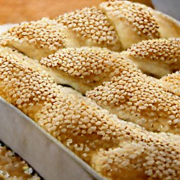 the brush is dipped in the egg wash mixture and then brushed on the loaf bread. the loaf bread is then sprinkled with sesame seeds.