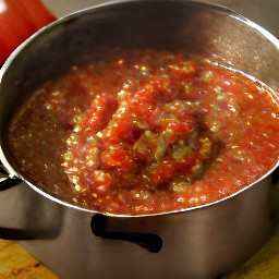 a saucepan full of tomatoes, onions, jalapeno peppers, green bell peppers, garlic, vinegar, tomato sauce, chili powder, cumin and garlic powder with 3 tbsp of salt stirred in.