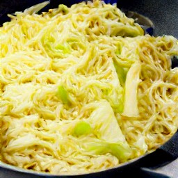 the egg noodles, caraway seeds, and salt are transferred to the wok and cooked for 5 minutes on low heat. the fried cabbage and noodles are then transferred to a plate.