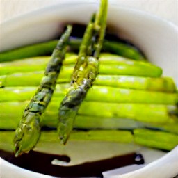 a bowl of balsamic vinegar, lemon juice, 1 tbsp olive oil, soy sauce, and minced garlic mixed together with asparagus. the asparagus has been marinated for 30 minutes.
