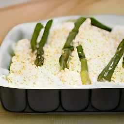 the bowl's contents, trimmed asparagus, and grated parmesan cheese have been added to the ovenproof dish.