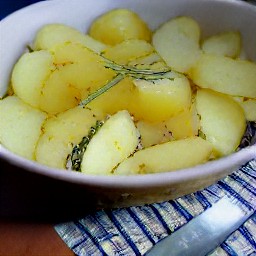 a bowl of potato halves mixed with olive oil, rosemary, and garlic, with salt and black pepper to taste.