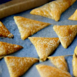 triangles of puff pastry on a baking sheet with the other half of the egg mixture brushed on top.