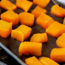 a baking sheet with butternut squash cubes spread over it, coated in olive oil.