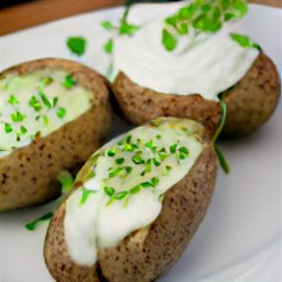 a platter of baked potatoes with sour cream and chopped chives on top.