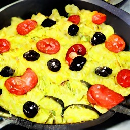 a dish of scrambled eggs with onions, zucchini, tomatoes, and olives.