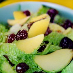 a salad with lettuce, swiss cheese, cashew nuts, dried cranberries, apples and pears. the salad is then drizzled with lemon poppy seed dressing and mixed together.