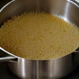 3 cups of boiling water with orzo pasta cooked in it.