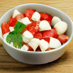 the output is a bowl of chopped tomatoes, mozzarella cheese cubes, chopped spring onions, dried cilantro, garlic powder, black pepper and the remaining salt. the mixture is drizzled with olive oil and lemon juice.