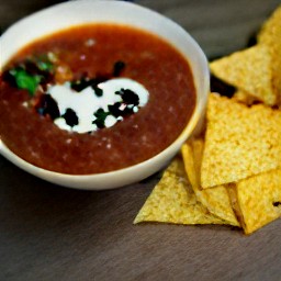 a bowl of soup with sour cream and crushed tortilla chips on top.