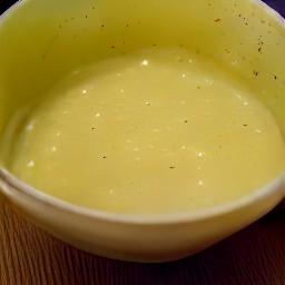 a bowl of yellow mustard with minced garlic, yeast flakes, and almonds mixed in, as well as 1 tbsp water, soy sauce, olive oil, lemon juice, and black pepper.