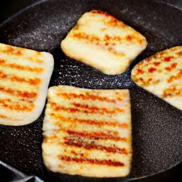 flipping the semi-fried halloumi cheese using a spatula.