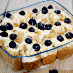 a glass baking dish with butter, bread cubes, cream cheese, blueberries, and the rest of the bread.