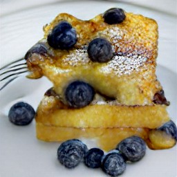 a plate of sliced blueberry french toast with a quarter cup of maple syrup over it.