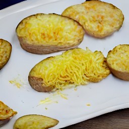 a cookie sheet with russet potato slices in a single layer, drizzled with the melted butter. the potatoes are sprinkled with salt, black pepper, and garlic powder. the shredded parmesan cheese