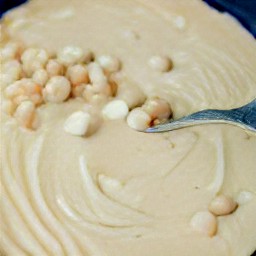 a bowl of batter containing butter, brown sugar, vanilla extract, and granulated sugar mixed together with eggs, flour mixture, chocolate chips, flaked coconut, and chopped macadamia nuts.