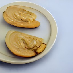 two apple halves with crunchy peanut butter spread on them, placed on a plate.