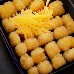 a casserole dish with tater tots and shredded cheddar cheese on top.