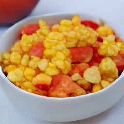 a large bowl containing olive oil, tomatoes, sweetcorn, coriander, lime zest, chili pepper and onions.