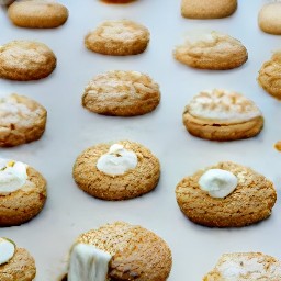 there 8 ginger nut biscuits on the baking sheet, each with a marshmallow on top.
