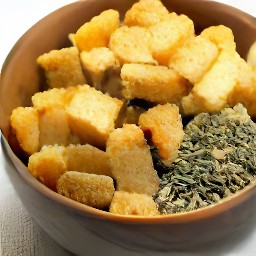 a bowl of bread cubes mixed with olive oil, dried basil, garlic, and salt.