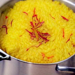 taking out the cloves and cinnamon stick from the cooked saffron rice, then fluffing it with a fork.