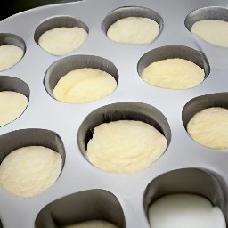 12 greased muffin cups in a tin, with batter poured into each cup.