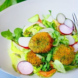 there should be raisins, carrots, zucchini, radishes, watercress, arugula, and spinach in a serving bowl. the bowl should have half a tbsp of canola oil and white vinegar stirred in with