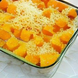 a baking dish with butternut squash cubes, salt, black pepper, cheese-herb mixture and chopped butter on top.