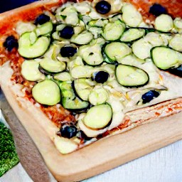 a pizza with sauce, mozzarella and parmesan cheese, onions, bell peppers, zucchini, black olives, tomatoes, garlic, dried basil oregano and 1/2 tsp of