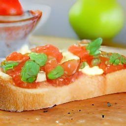 a toasted bread with pesto, tomato mixture, and cheese slices.