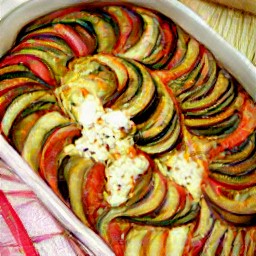 a ratatouille dish topped with cheese sauce and goat cheese, with zucchinis and olive oil.