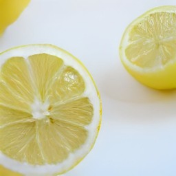 three-quarters of the lemons being cut in half and then squeezed using a squeezer, and the rest of the lemons being sliced.