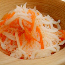 a bowl of shredded cabbage, grated carrots, apples slices, celery sticks slices, chopped parsley, pine nuts, pumpkin seeds, flaxseeds and sunflower seeds.