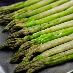 a baking sheet with asparagus and garlic mixture on it.