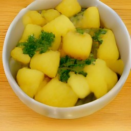 the transfer of the spicy potatoes to a serving bowl, then the scattering of 1 tsp of chopped coriander on top.