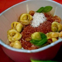 a bowl of pasta with spaghetti sauce, water, basil, stuffed spinach and ricotta tortellini.