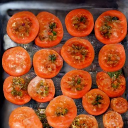 a baking sheet with tomato slices that have been drizzled with olive oil and sprinkled with kosher salt, black pepper, granulated sugar, and thyme leaves.