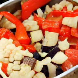 a roasting tin with red bell peppers, garlic, onions, eggplants, and tomatoes mixed with the dressing.
