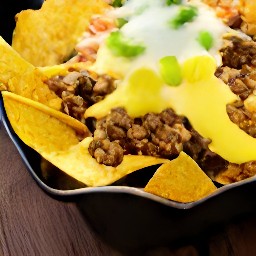 a dish of tortilla chips topped with the cooked meatless burger patties mixture and queso sauce.