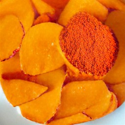a bowl of sweet potatoes mixed with chili powder, cumin, paprika, cayenne pepper, salt, black pepper and olive oil.
