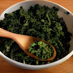 a bowl of chopped kale that is coated with olive oil and lime juice.