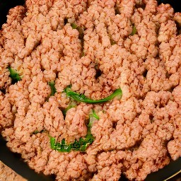 the meatless burger patties are crumbled with a wooden spoon.