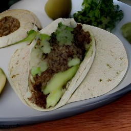 a plate of tortillas with tomatillo salsa, cooked beyond beef crumbles, sliced avocados, cilantro, and lime juice.