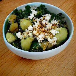 a bowl of roasted potatoes, kale mix, and avocado dressing topped with crumbled feta cheese and chili flakes.