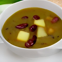 a bowl of soup containing olive oil, garlic, kidney beans, vegetable broth, zucchini, peas, pesto and salt.